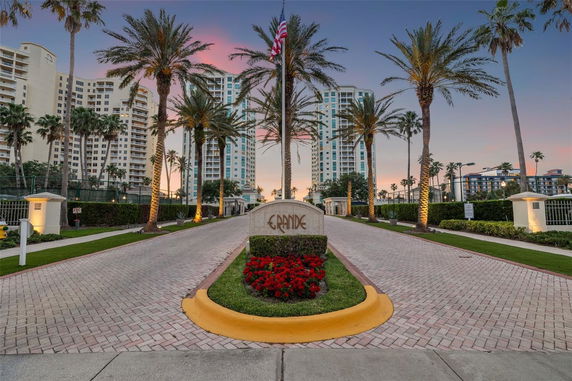 Front view of a large multi-story residential building complex with palm trees and landscaped entrance.