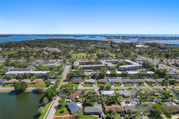 Aerial panoramic view of a residential and commercial area with houses, buildings, roads, and water bodies in the background.