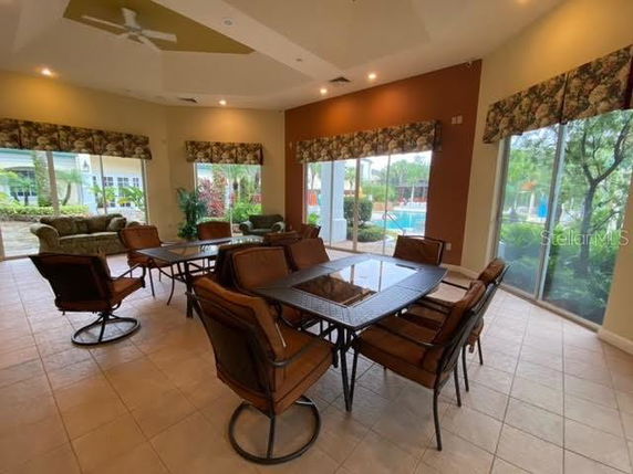 Indoor view of a clubhouse with tables and chairs placed near large windows showing an outdoor pool area.