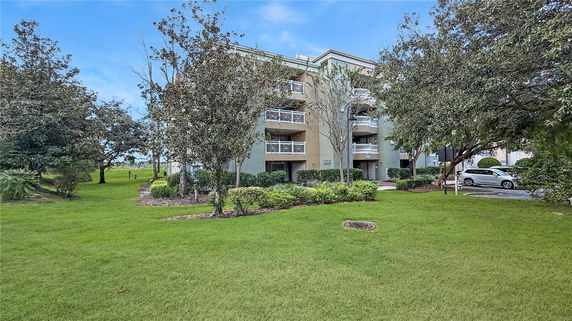 Front view of a multi-story residential building with balconies surrounded by trees and greenery.