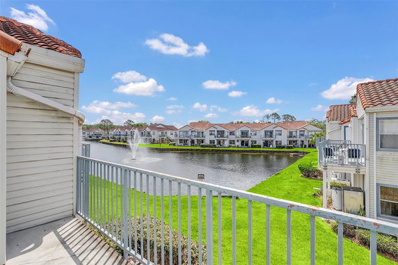 View from a building balcony overlooking a lake with water fountain and surrounding residential houses.