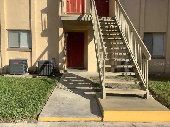 Front view of a building with stairs leading to an upper floor and visible air conditioning units.