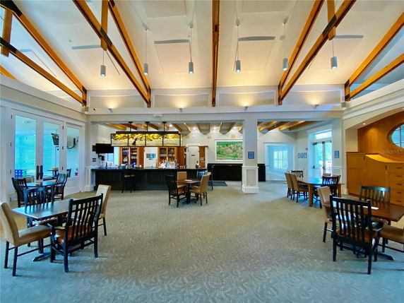 Interior view of a clubhouse with tables, chairs, and a bar area.