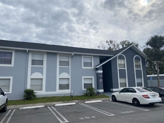 Front view of a two-story residential building with a gable roof and parking area in front.