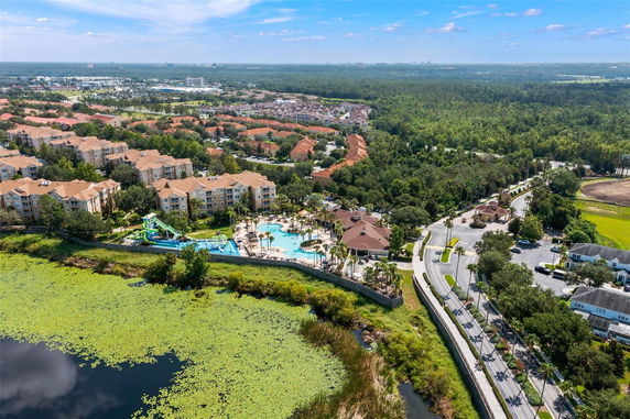 Aerial view of a residential community with tan-colored buildings, a large swimming pool, and green landscape.