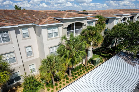 Front view of a multi-story apartment building with a tiled roof and palm trees.