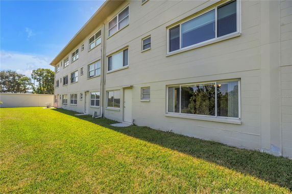 Side view of a three-story building with multiple windows and a grassy lawn in the foreground.