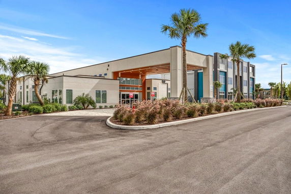 Front view of a modern multi-story building with large windows and palm trees.