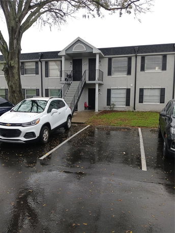 Front view of a two-story residential building with a central staircase and parked cars in front.
