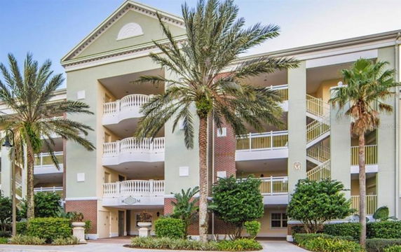 Front view of a multi-story residential building with balconies and surrounded by palm trees.