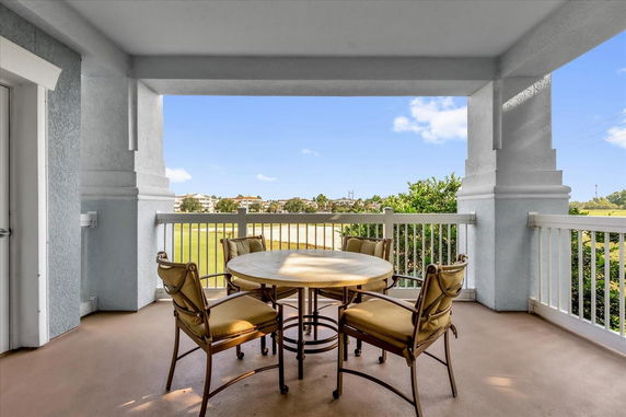 Outdoor patio area with a round table and four chairs, overlooking a grassy field with buildings in the distance.