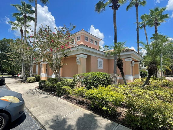 Front view of a single-story pink house with a small upper-level section, surrounded by palm trees.