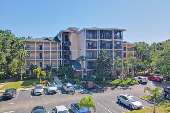 Front view of a multi-story residential building with balconies and a parking area in front.