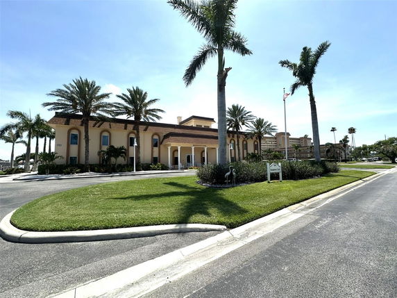 Front view of a large beige building with arches and palm trees.