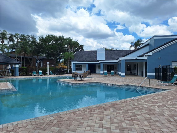 Swimming pool area with surrounding building and deck chairs.