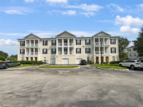 Front view of a three-story residential building with multiple balconies and parking area at the front.