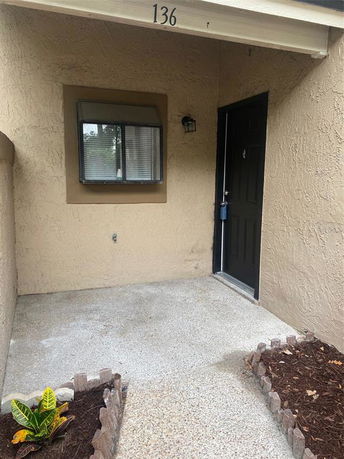 Front view of an entrance to a tan-colored building with a black door and a small window.