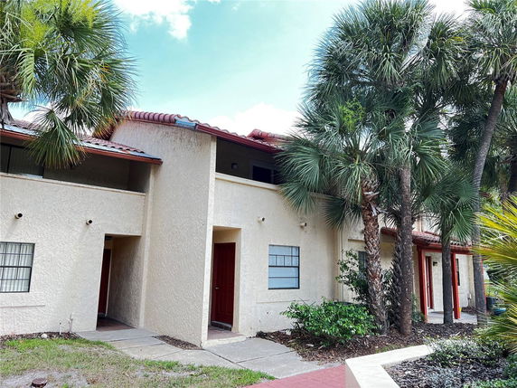 Front view of a two-story building with red doors and tiled roof, surrounded by palm trees.