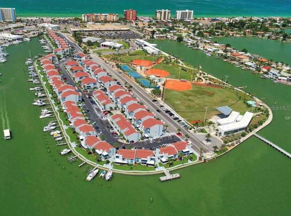 Aerial panoramic view of a coastal community with rows of houses, surrounded by water, and boats docked along the shore.