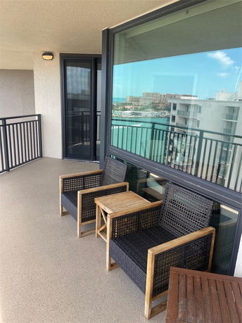 Balcony with seating and railing, overlooking buildings and water in the distance.