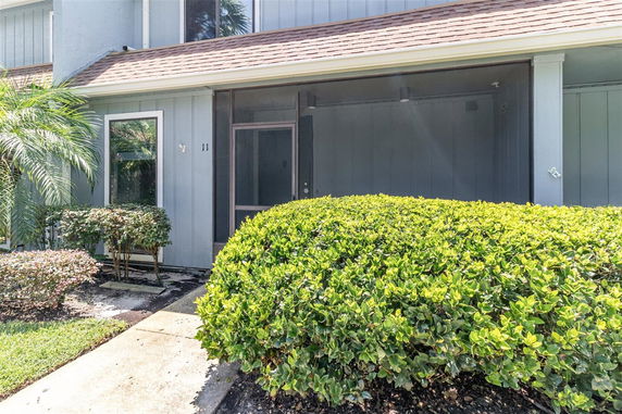 Front view of a house with large bushes, windows, and a screen door entrance.