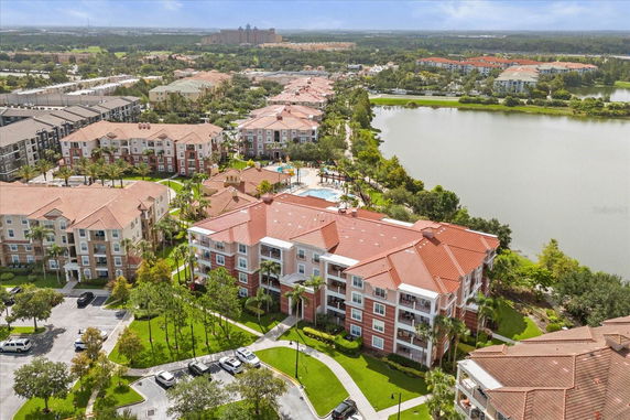 Aerial view of multiple multi-story buildings with red roofs, a swimming pool, and surrounding greenery near a lake.