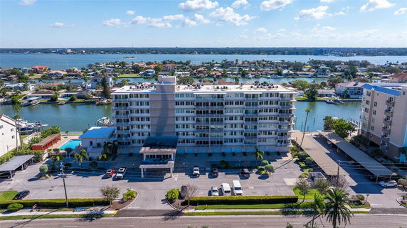 Front view of a multi-story residential building with water and houses in the background.