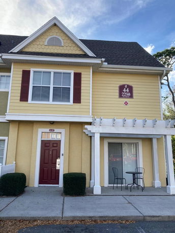 Front view of a two-story yellow house with a red door and a small covered patio.