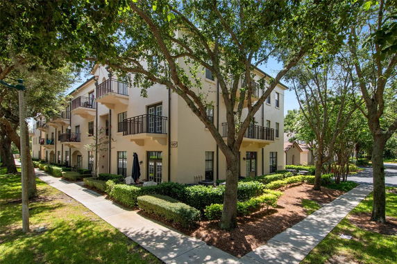 Front view of a multi-story residential building with balconies and surrounding greenery.