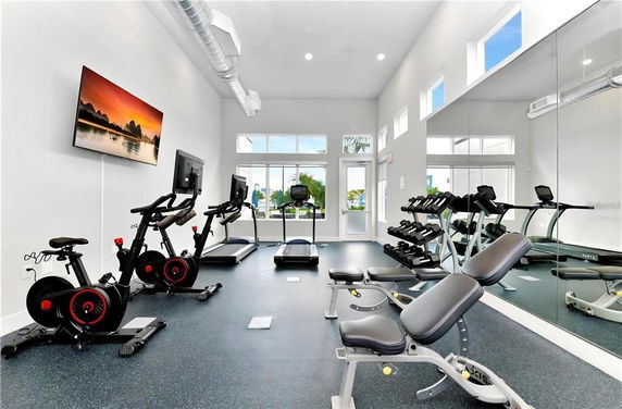 Interior view of a gym with exercise bikes, treadmills, weights, and a wall-mounted television.