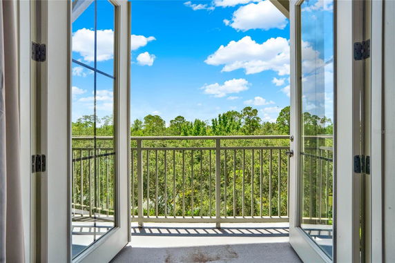 View from a balcony overlooking a green landscape with trees and a blue sky.