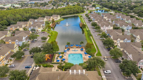 Aerial view of a residential community with a swimming pool, surrounding houses, and a central lake with a fountain.