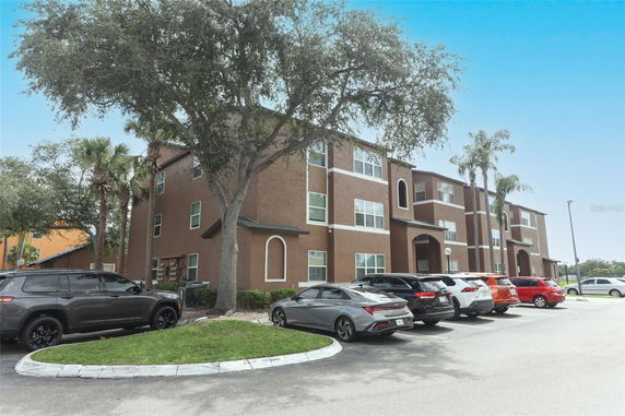 Front view of a multi-story brown apartment building with parking area.