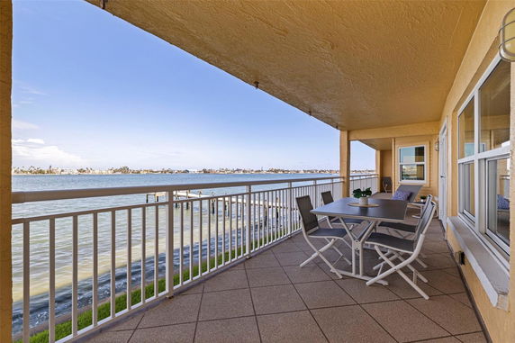 Covered balcony with outdoor seating overlooking a body of water.