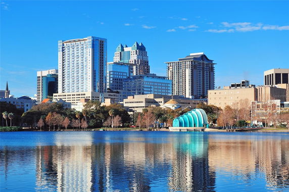 City skyline with tall buildings and a reflective lake in the foreground.