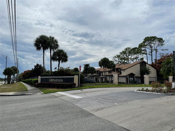 View of a residential building with a gated entrance and surrounding palm trees.