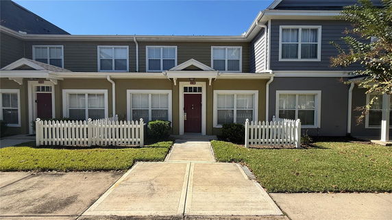 Front view of a two-story townhouse with a small front yard and white picket fence.