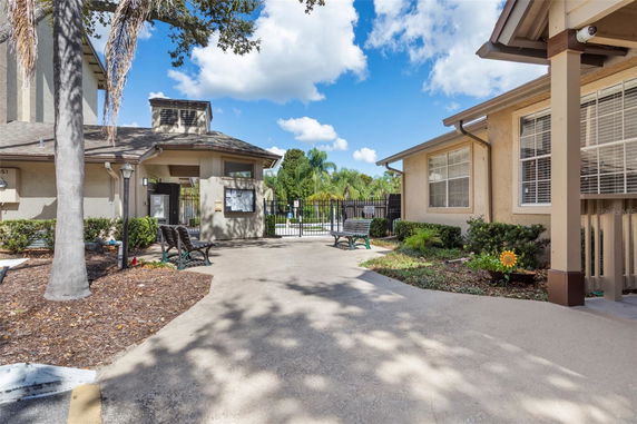 View of a single-story building with a gabled roof and light-colored exterior, featuring benches and a fenced area in the background.