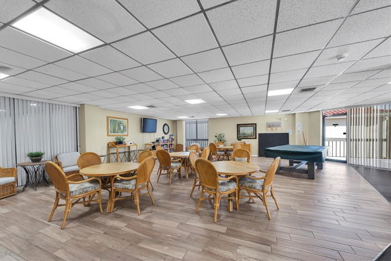 Interior view of a recreational room with tables and chairs, a pool table, and wall decor.