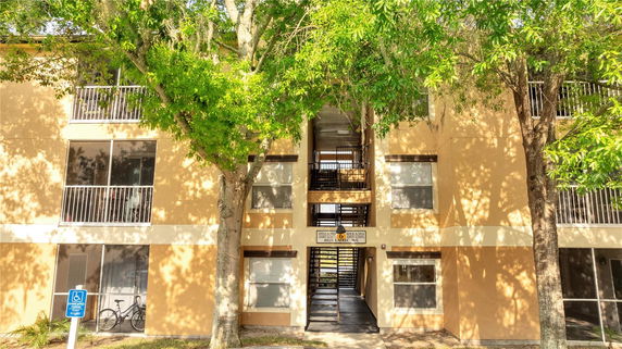 Front view of a multi-story apartment building with balconies and shaded by trees.