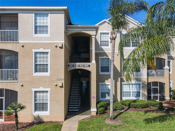 Front view of a multi-story apartment building with balconies and an entrance walkway.
