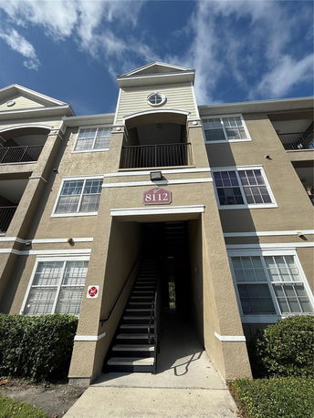 Front view of a multi-story residential building with balconies and a central staircase entrance.