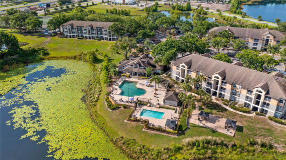 Panoramic view of an apartment complex with swimming pools near a pond.