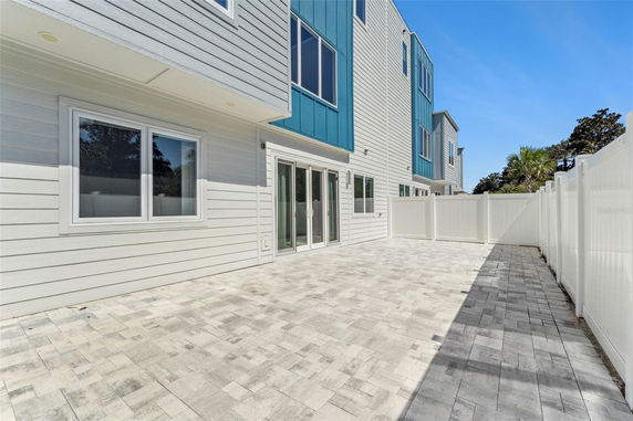 Rear view of a multi-story house with sliding glass doors and windows, featuring a paved courtyard and white fence.