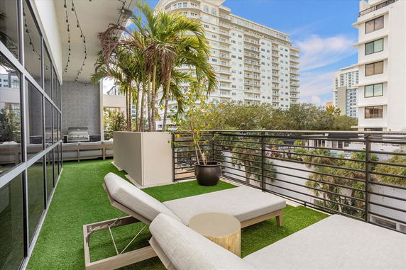 Rooftop with artificial grass, lounge chairs, and potted plants, showing nearby buildings in the background.