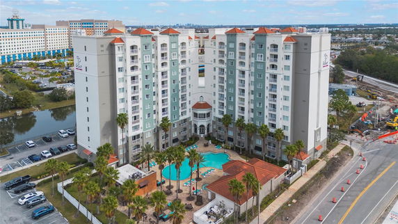 Front view of a large multi-story building with a central swimming pool and palm trees.