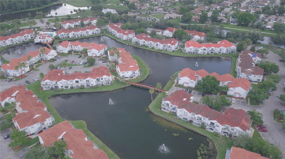 Aerial view of a residential complex with red-roofed buildings surrounding small lakes and fountains.