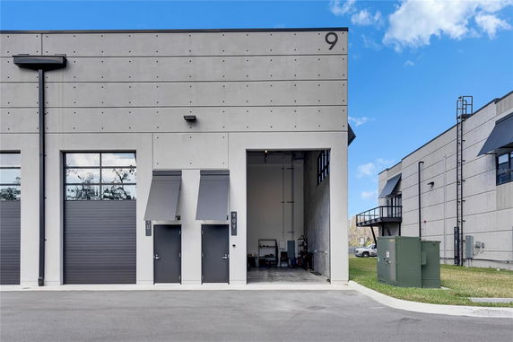 Front view of a grey industrial building with large garage doors and wall-mounted awnings.
