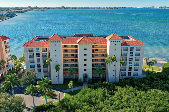 Front view of a multi-story residential building with red tile roofing, located near a waterfront.