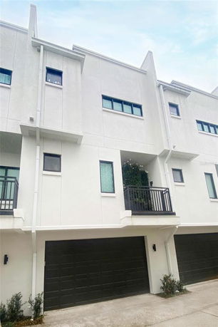 Front view of a modern three-story townhouse with a balcony and double garage.